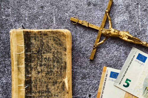 © Marcin Łazarczyk - stock.adobe.com Foto: Kreuz, Buch und Geldscheine